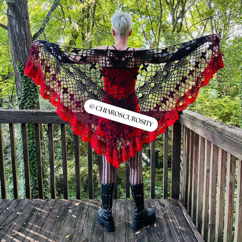 May include: A black and red crochet shawl with a floral design. The shawl has a scalloped edge and is displayed outdoors. The text "CHIAROSCUROSITY" is visible on the shawl.