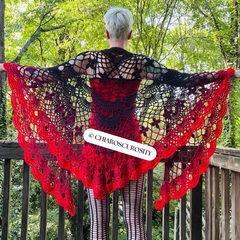 May include: A handmade, open-weave shawl in black, red, and purple. The shawl features a floral pattern and a scalloped edge. The text "&copy; CHIAROSCUROSITY" is visible on the shawl.