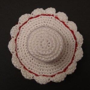 May include: White crocheted sun hat with a red trim and a scalloped edge.