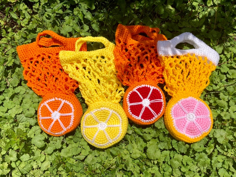 Puede incluir: Cinco bolsas de frutas de ganchillo de color naranja, amarillo y rosa con malla blanca. Las bolsas est&aacute;n hechas para parecerse a naranjas, pomelos y un pomelo rosa.