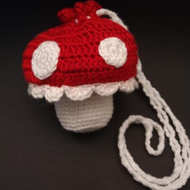 May include: A crocheted mushroom-shaped bag with a white strap. The bag is red with white polka dots and a white crocheted trim.