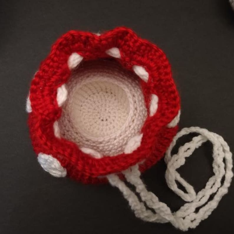 May include: A red and white crocheted drawstring bag shaped like a mushroom. The bag has a white crocheted drawstring.