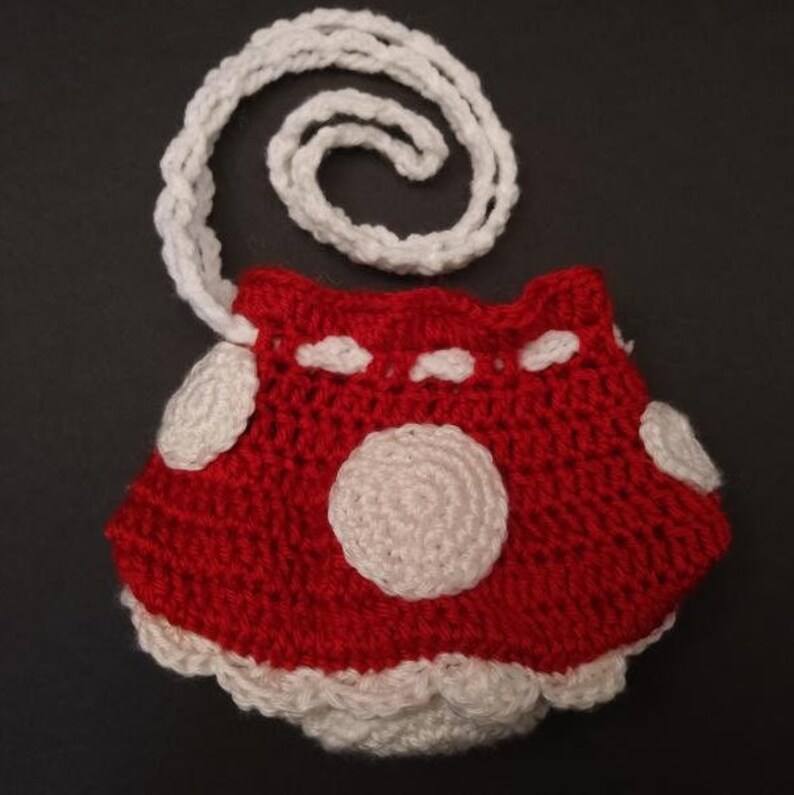 May include: A red and white crocheted mushroom-shaped purse with a white crocheted strap.