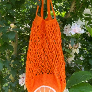 Puede incluir: Bolsa de malla de crochet naranja con un dise&ntilde;o de rodaja de naranja de crochet. La bolsa tiene un asa larga y est&aacute; hecha de un hilo naranja brillante.