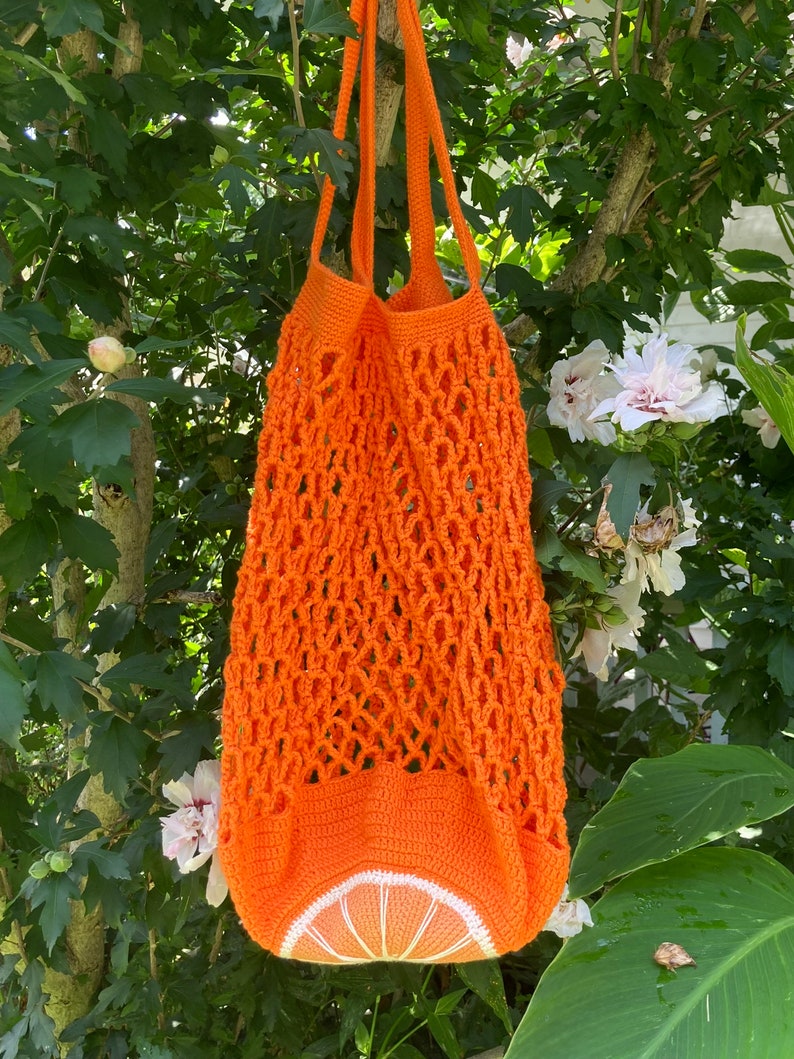 Puede incluir: Bolsa de malla de crochet naranja con un dise&ntilde;o de rodaja de naranja de crochet. La bolsa tiene un asa larga y est&aacute; hecha de un hilo naranja brillante.