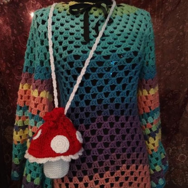 May include: A rainbow crochet top with a white crocheted mushroom purse. The purse has a red top with white polka dots and a white crocheted stem.