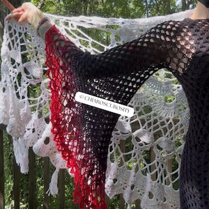 May include: A long-sleeved crochet top featuring a black bodice and sleeves that transition into a vibrant red gradient at the flared cuffs. A white, intricate, large-scale crochet shawl with a skull motif is draped behind. Text reads CHIAROSCUROSITY.