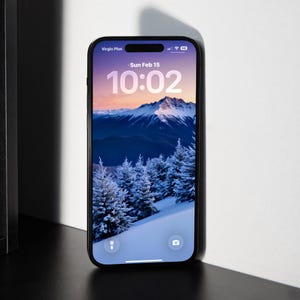 May include: A black smartphone shows a winter scene wallpaper with snow-covered trees and mountains under a pink and blue sky. The screen displays the time as 10:02 and the date as Sun Feb 15. The phone is labelled "Virgin Plus" at the top.