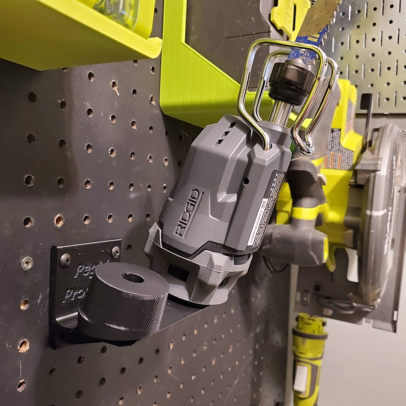 May include: A black wall-mounted tool holder with a gray and black reciprocating saw attached. The saw has a silver hook and the brand name "RIDGID" is visible on the side.