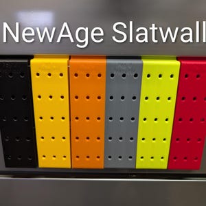 Puede incluir: Una fila de accesorios de paneles ranurados de colores en negro, amarillo, naranja, gris, verde lima y rojo. Cada accesorio tiene múltiples agujeros espaciados uniformemente. El texto "NewAge Slatwall" se muestra en la parte superior.