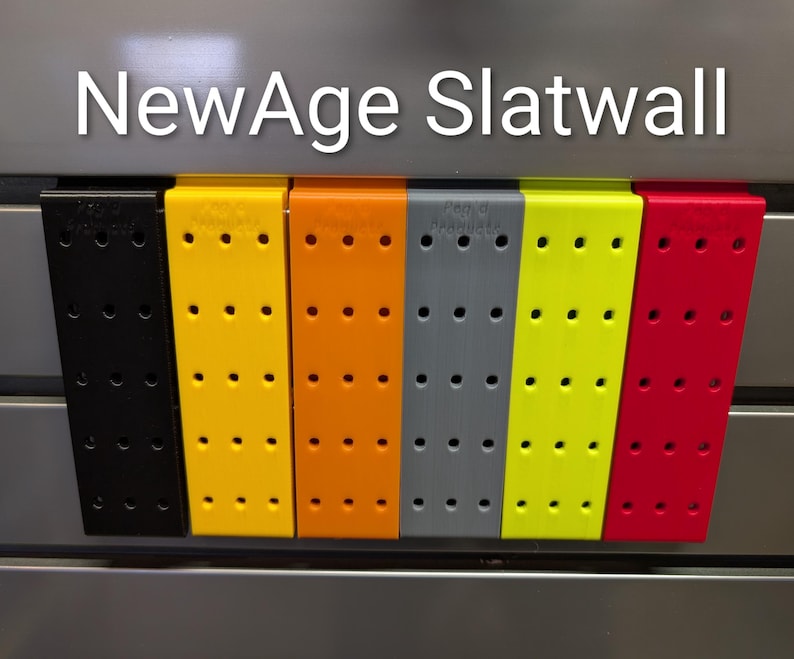 Puede incluir: Una fila de accesorios de paneles ranurados de colores en negro, amarillo, naranja, gris, verde lima y rojo. Cada accesorio tiene m&uacute;ltiples agujeros espaciados uniformemente. El texto "NewAge Slatwall" se muestra en la parte superior.