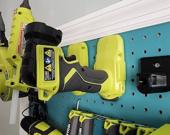 Pode incluir: Um painel de pinos turquesa com várias ferramentas elétricas penduradas nele. As ferramentas incluem uma furadeira sem fio verde e preta, uma chave de impacto sem fio verde e preta, uma pistola de cola sem fio verde e preta e um suporte para ferramentas elétricas preto.