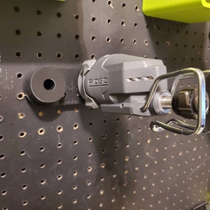 May include: A gray Ridgid power tool with a black handle and a silver hook hanging on a pegboard.