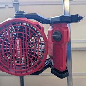 May include: A red and black Craftsman portable fan featuring a circular grille with the brand name embossed in the centre. The device includes a side-mounted control knob and a black adjustable clamp mechanism attached to a vertical metal pole.