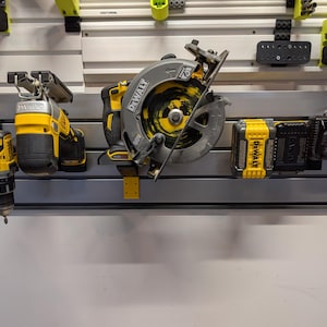 Puede incluir: Una colecci&oacute;n de herramientas el&eacute;ctricas amarillas y negras, incluyendo una sierra circular, un taladro y bater&iacute;as, montadas en una pared. Las herramientas son de la marca DeWalt y se exhiben contra una pared blanca con varios accesorios de almacenamiento.