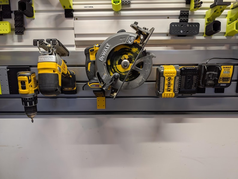 Puede incluir: Una colecci&oacute;n de herramientas el&eacute;ctricas amarillas y negras, incluyendo una sierra circular, un taladro y bater&iacute;as, montadas en una pared. Las herramientas son de la marca DeWalt y se exhiben contra una pared blanca con varios accesorios de almacenamiento.
