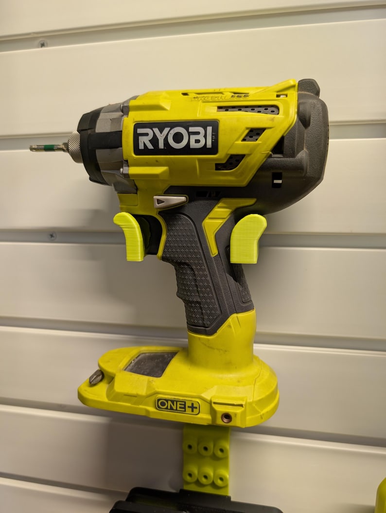 May include: A yellow and black Ryobi impact driver with the text "RYOBI" on the side. The drill is cordless and has a black grip. The drill is mounted on a wall.