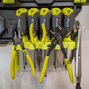 May include: A wall-mounted tool organizer with six yellow and black screwdrivers and five yellow and black pliers. The organizer is labeled "RYOBI" on each screwdriver.