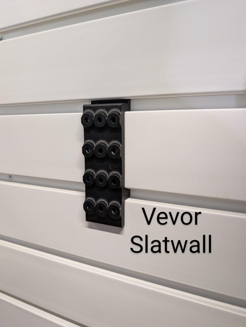 Puede incluir: Primer plano de un panel de listones blanco con un soporte negro. El soporte tiene m&uacute;ltiples agujeros circulares. El texto "Vevor Slatwall" est&aacute; impreso en el panel de listones.