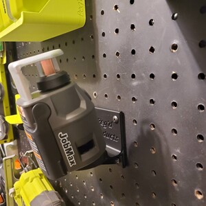 May include: A black JobMax battery is mounted on a black pegboard with a black metal bracket. The bracket has the text "Reg'd Products" on it.