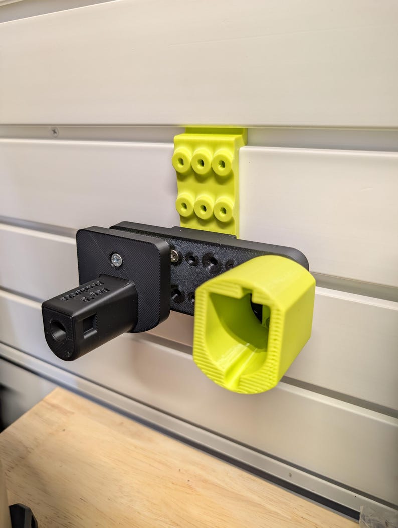 Puede incluir: Un sistema de almacenamiento montado en la pared con un dise&ntilde;o impreso en 3D en negro y amarillo. El sistema incluye un soporte negro con texto y un soporte amarillo. Un soporte amarillo est&aacute; montado encima de los soportes.