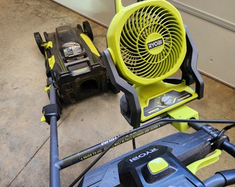 Peut inclure: Une tondeuse à gazon noire et verte avec une poignée noire et un bouton jaune. La tondeuse est reliée à un souffleur de feuilles vert et noir avec un ventilateur jaune et une poignée noire. Le souffleur de feuilles a un panneau de commande avec le texte "RYOBI" et "WRAPTEK" dessus. Le texte "PRIOR TO USE - MUST BE FULLY EXTENDED AND LOCKED" est imprimé sur la poignée de la tondeuse.
