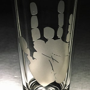 Puede incluir: Un vaso de beber de vidrio transparente con un diseño esmerilado de una mano haciendo el gesto de rock and roll.