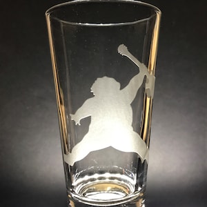 Puede incluir: Un vaso de cerveza de vidrio transparente con una silueta blanca de una persona tocando la guitarra grabada en el lateral.