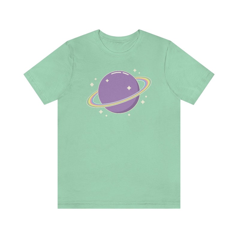 K&ouml;nnte beinhalten: Ein hellgr&uuml;nes T-Shirt mit einem lila Planeten mit einem Regenbogenring darum. Der Planet ist von kleinen wei&szlig;en Sternen umgeben.