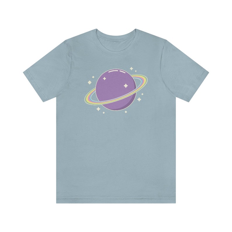 K&ouml;nnte beinhalten: Ein hellblaues T-Shirt mit einem lila Planeten mit einem Regenbogenring darum. Der Planet ist von kleinen wei&szlig;en Sternen umgeben.