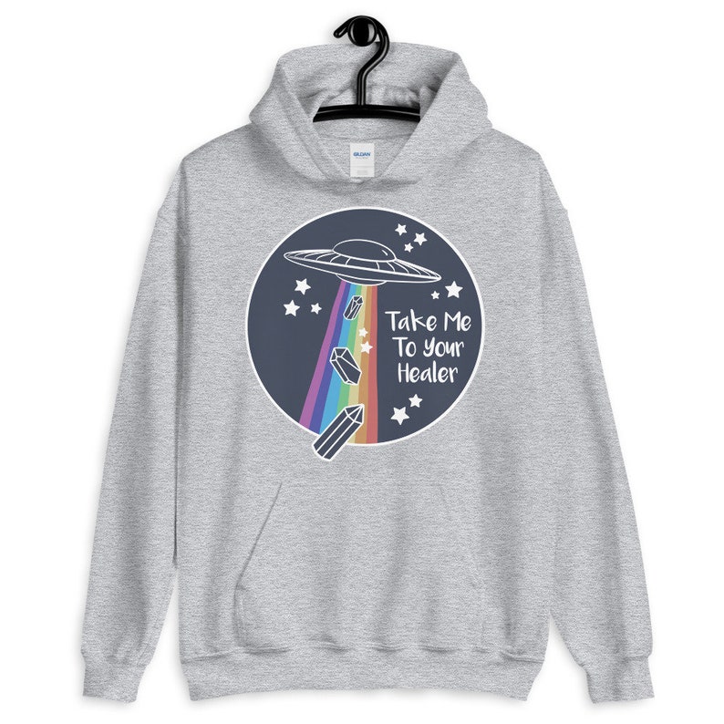 May include: A gray hoodie with a graphic of a UFO flying over a rainbow with crystals falling from it. The text "Take Me To Your Healer" is written below the UFO.