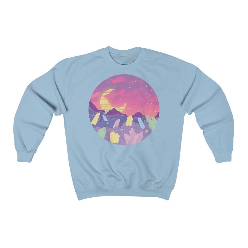 May include: Light blue sweatshirt with a circular graphic of a crescent moon, mountains, and a pink and purple sunset. The graphic is surrounded by a ring of pastel-colored crystals.