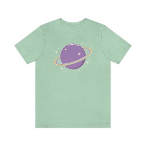 K&ouml;nnte beinhalten: Ein hellgr&uuml;nes T-Shirt mit einem lila Planeten mit einem Regenbogenring darum. Der Planet hat ein paar wei&szlig;e Sterne drumherum.