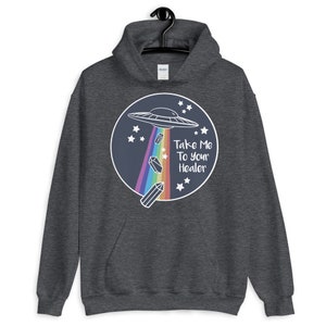 May include: A dark grey hoodie with a graphic of a UFO flying over a rainbow with crystals falling from it. The text "Take Me To Your Healer" is written in white on a blue circle.