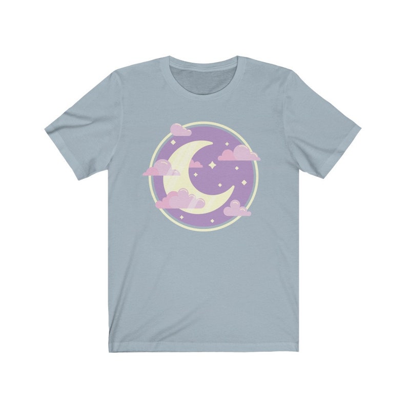 May include: A light blue t-shirt with a purple circle design featuring a crescent moon and pink clouds. The moon is yellow and there are small white stars inside the circle.