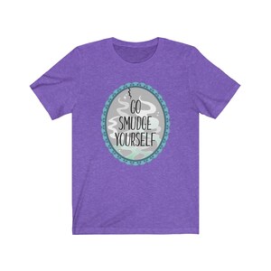 以下が含まれることがあります： 紫色の半袖Tシャツに、青と白の円形のデザインが施され、「GO SMUDGE YOURSELF」と書かれています。