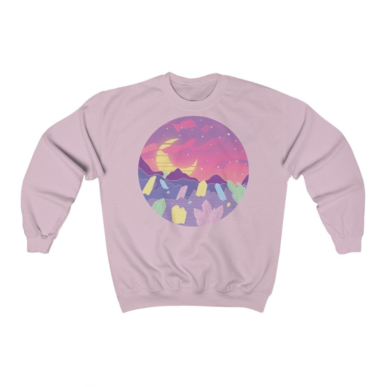 May include: A pink sweatshirt with a graphic of a crescent moon, mountains, and crystals in a circle against a sunset background.