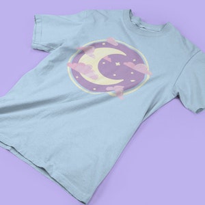 May include: A light blue t-shirt with a graphic of a crescent moon and clouds in pastel pink and purple.