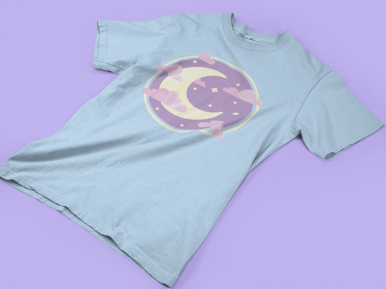 May include: A light blue t-shirt with a graphic of a crescent moon and clouds in pastel pink and purple.