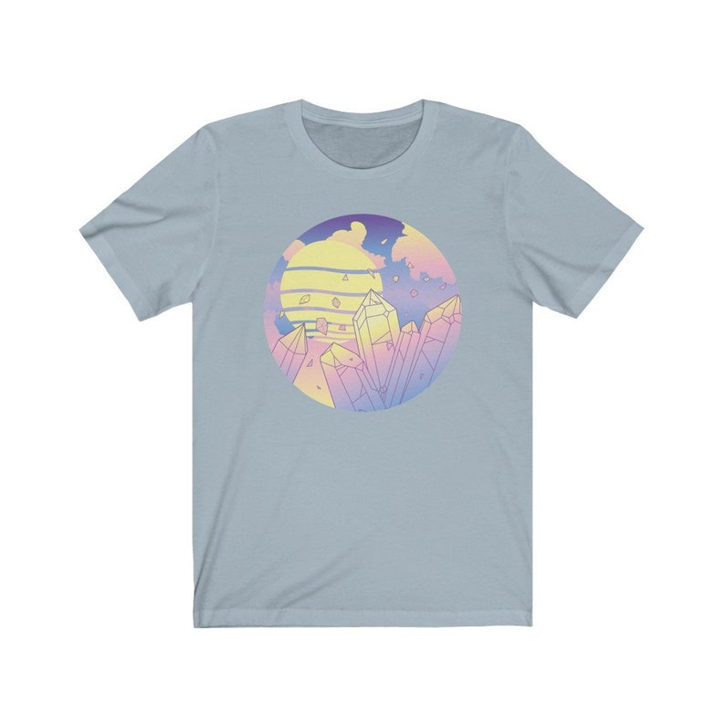 May include: A light blue t-shirt with a graphic of a sunset and crystals in a circle. The graphic is in pastel pink, yellow, and blue colors.