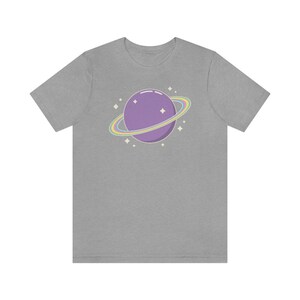 K&ouml;nnte beinhalten: Ein graues T-Shirt mit einem lila Planeten mit einem Regenbogenring darum. Der Planet hat ein paar wei&szlig;e Sterne drumherum.