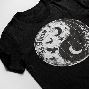 May include: Black t-shirt with a white yin yang symbol featuring the text "As Above, So Below" and a crescent moon on each side.