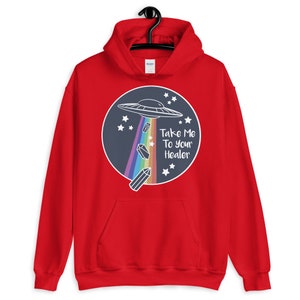 May include: Red hooded sweatshirt with a graphic of a UFO flying over a rainbow and crystals. The text "Take Me To Your Healer" is printed on the graphic.