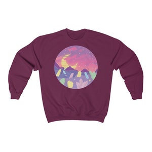 May include: A maroon sweatshirt with a circular graphic of a crescent moon, mountains, and crystals in a pastel color palette against a pink and purple sunset.
