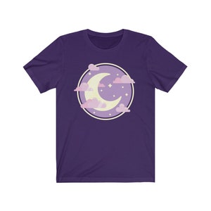 May include: Purple short-sleeved t-shirt with a graphic of a crescent moon in a circle with pink clouds and stars.