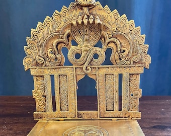 Puede incluir: Un trono de metal dorado con tallas intrincadas y un diseño de serpiente. El trono tiene una base cuadrada con cuatro patas y una plataforma elevada. El respaldo del trono es arqueado y presenta un diseño detallado de una serpiente con múltiples cabezas.