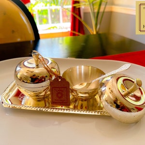 Puede incluir: Una bandeja plateada con dos recipientes con forma de manzana y un taz&oacute;n peque&ntilde;o con una cuchara. La bandeja est&aacute; decorada con un borde de cuentas. Los recipientes y el taz&oacute;n est&aacute;n hechos de metal pulido y tienen un acabado brillante. La bandeja est&aacute; sobre una superficie blanca. El logotipo de Golden Heritage est&aacute; en la esquina superior derecha de la imagen.