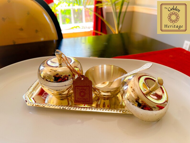Puede incluir: Una bandeja plateada con dos recipientes con forma de manzana y un taz&oacute;n peque&ntilde;o con una cuchara. La bandeja est&aacute; decorada con un borde de cuentas. Los recipientes y el taz&oacute;n est&aacute;n hechos de metal pulido y tienen un acabado brillante. La bandeja est&aacute; sobre una superficie blanca. El logotipo de Golden Heritage est&aacute; en la esquina superior derecha de la imagen.