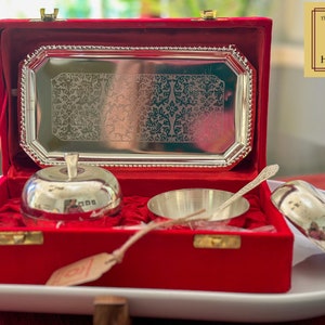 Puede incluir: Un juego de servicio de plata en una caja de terciopelo rojo. El juego incluye dos cuencos con forma de manzana, un cuenco peque&ntilde;o y una cuchara. La caja tiene una bandeja de plata con un dise&ntilde;o grabado. La caja tiene una etiqueta que dice "The Golden Heritage".
