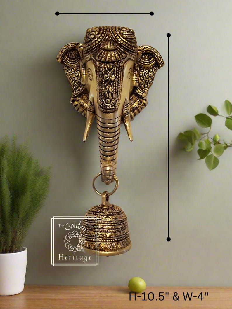 Puede incluir: Colgante de pared de metal dorado en forma de cabeza de elefante con detalles intrincados y una campana colgando del tronco. La cabeza de elefante mide 10,5 pulgadas de alto y 4 pulgadas de ancho.